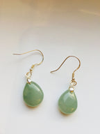 A pair of green jade teardrop earrings with silver hooks, displayed against a light background.