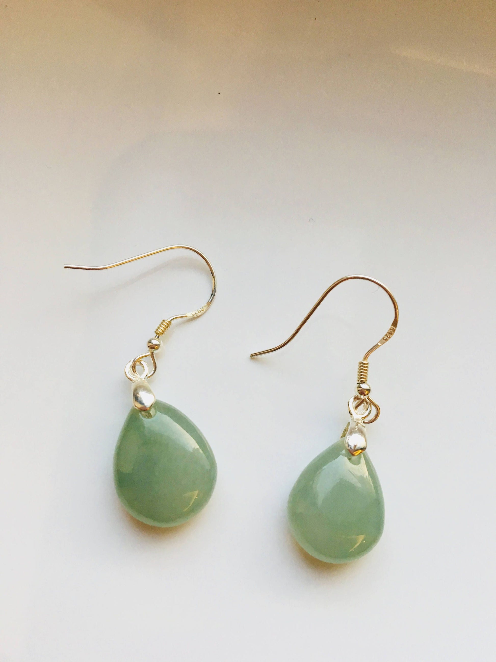 A pair of green jade teardrop earrings with silver hooks, displayed against a light background.