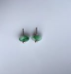 Pair of green round jade stud earrings on a light gray background side veiw