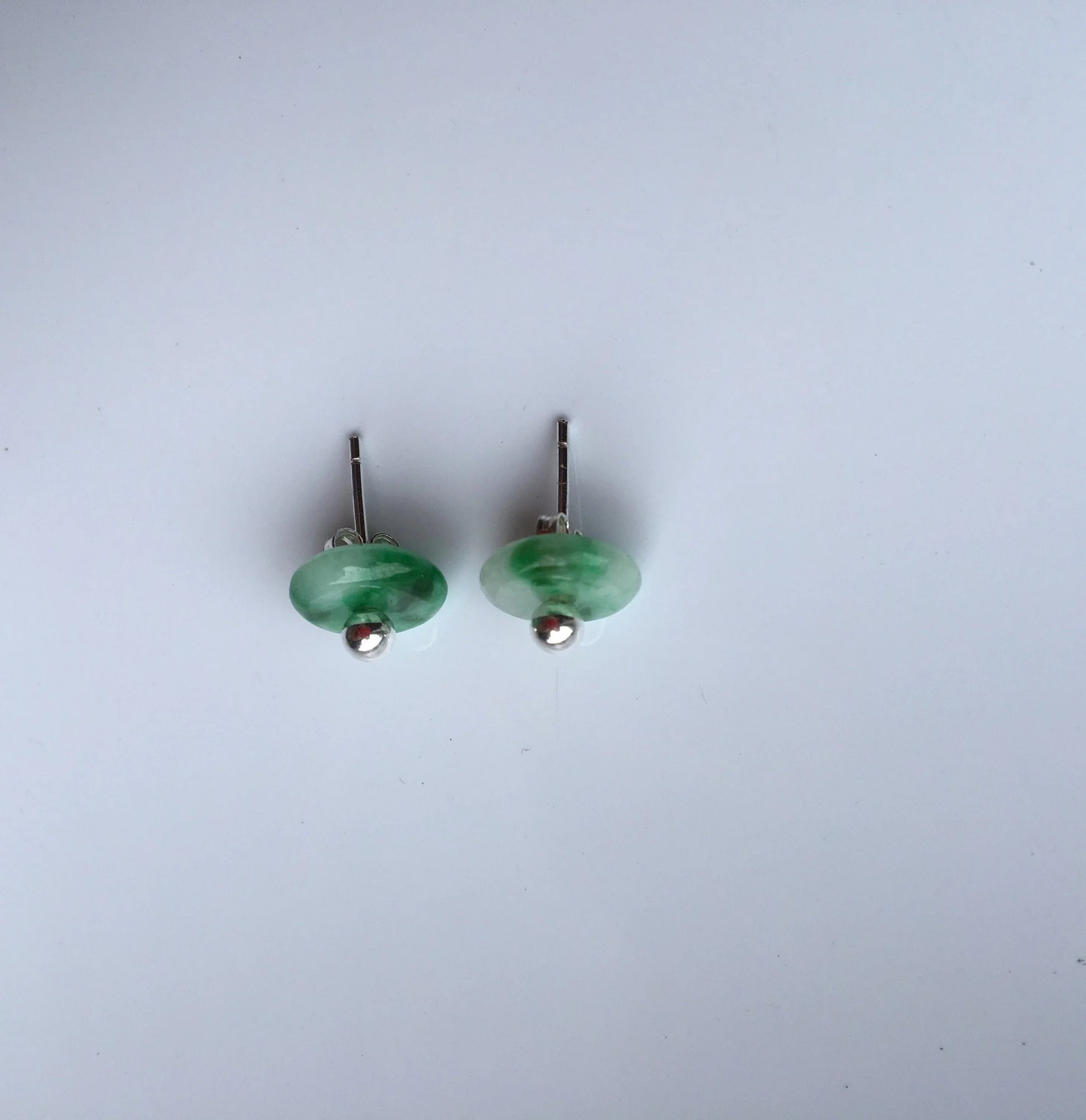 Pair of green round jade stud earrings on a light gray background side veiw