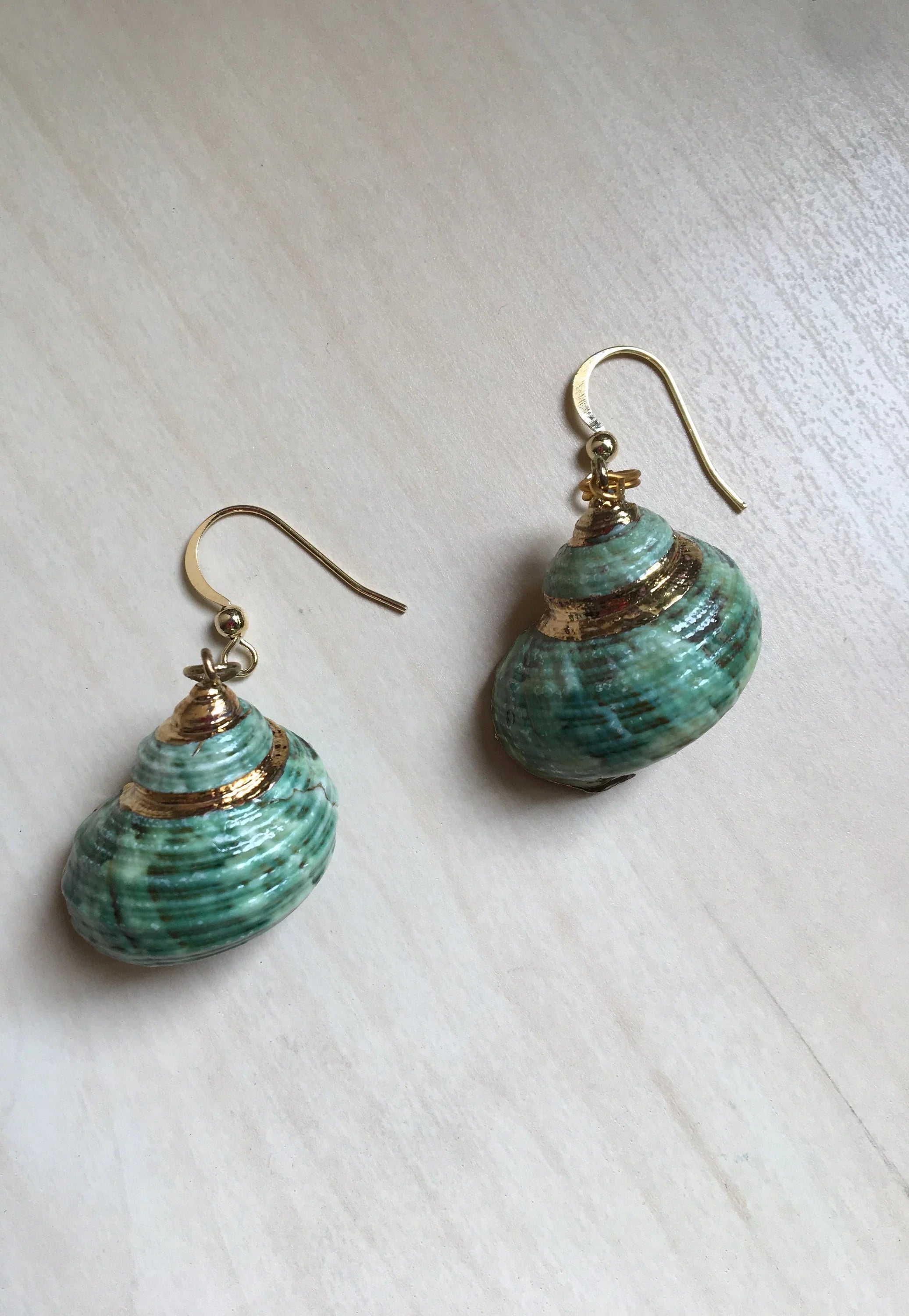 Pair of green shell earrings with gold accents on a light wooden surface