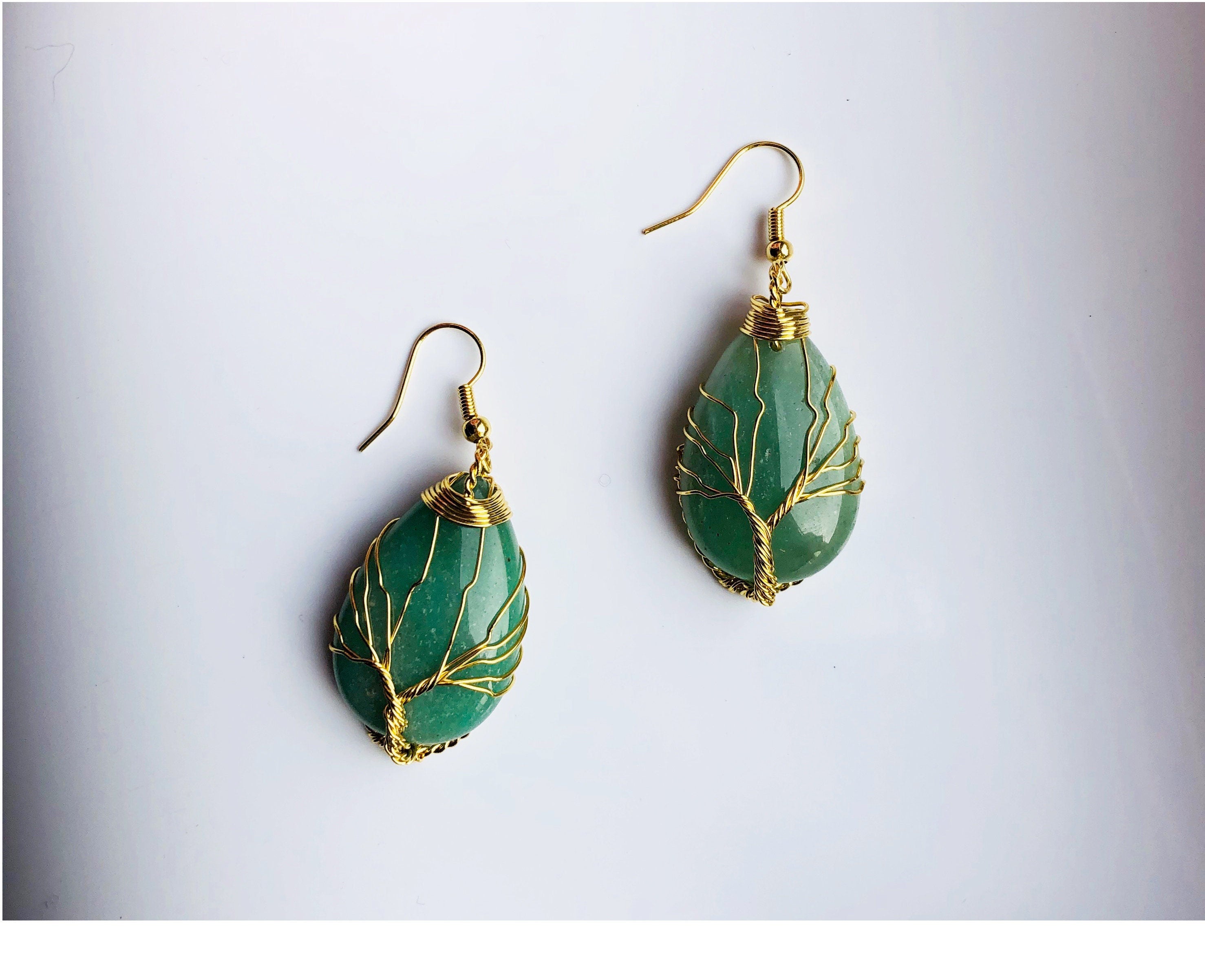 A pair of teardrop-shaped green jade earrings with gold wire wrapped around them, designed to represent a tree of life pattern.