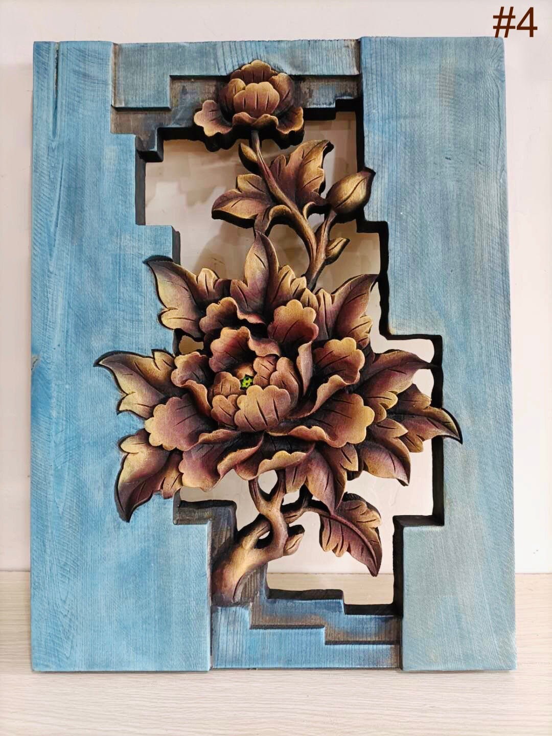 A hand-carved wooden art piece depicting a floral design with brown and white colors on a blue background, intended for tabletop presentation or wall hanging.