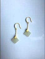 A pair of square white jade earrings with gold hooks, displayed against a light background.