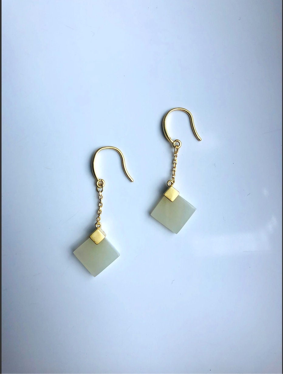A pair of square white jade earrings with gold hooks, displayed against a light background.