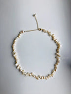 An irregular natural pearl necklace with gold-filled pearl beads. The necklace is white and gold in color, with an adjustable chain.