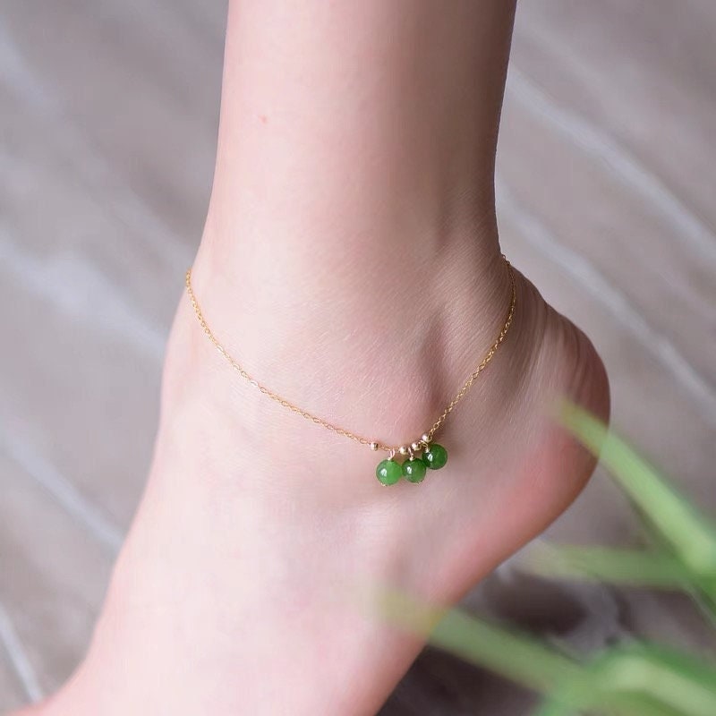A foot model wearing green jade anklet with gold chain on ankle, styled for elegant look