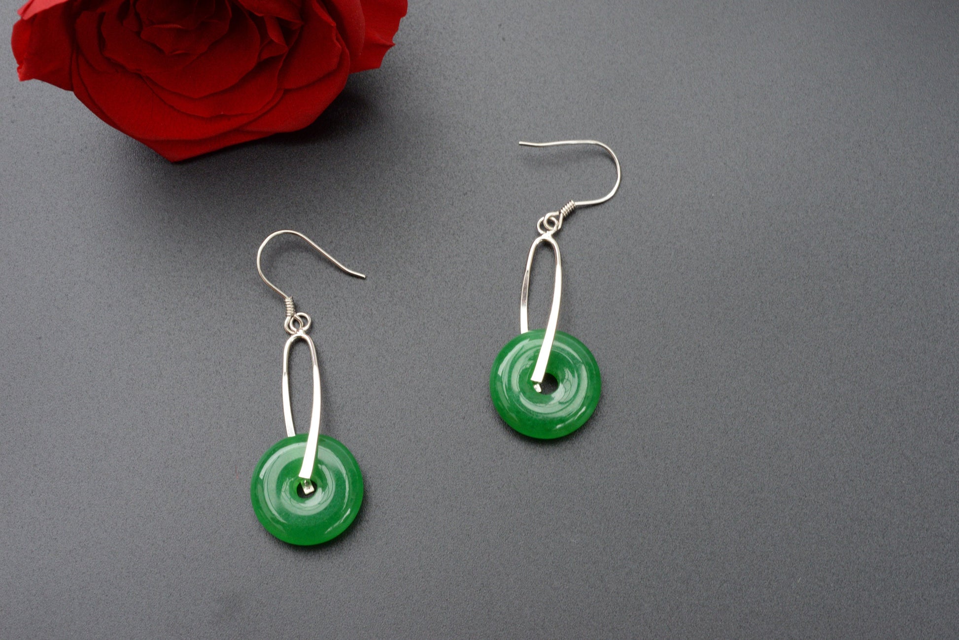 Round jade dangle earrings styled with black background and soft lighting for natural lifestyle feel and a red rose