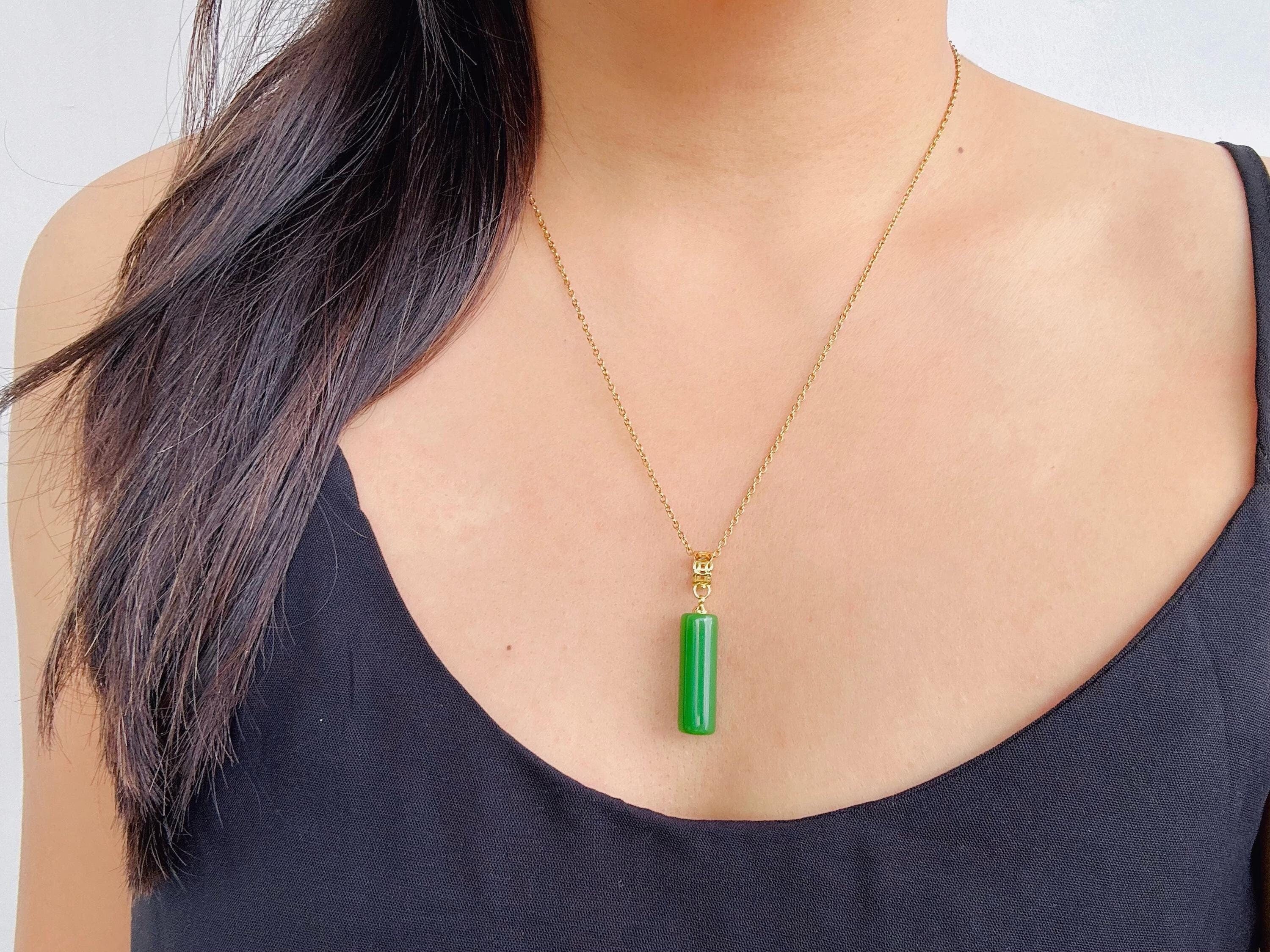 Model wearing long green jade pillar pendant with gold chain styled over black top