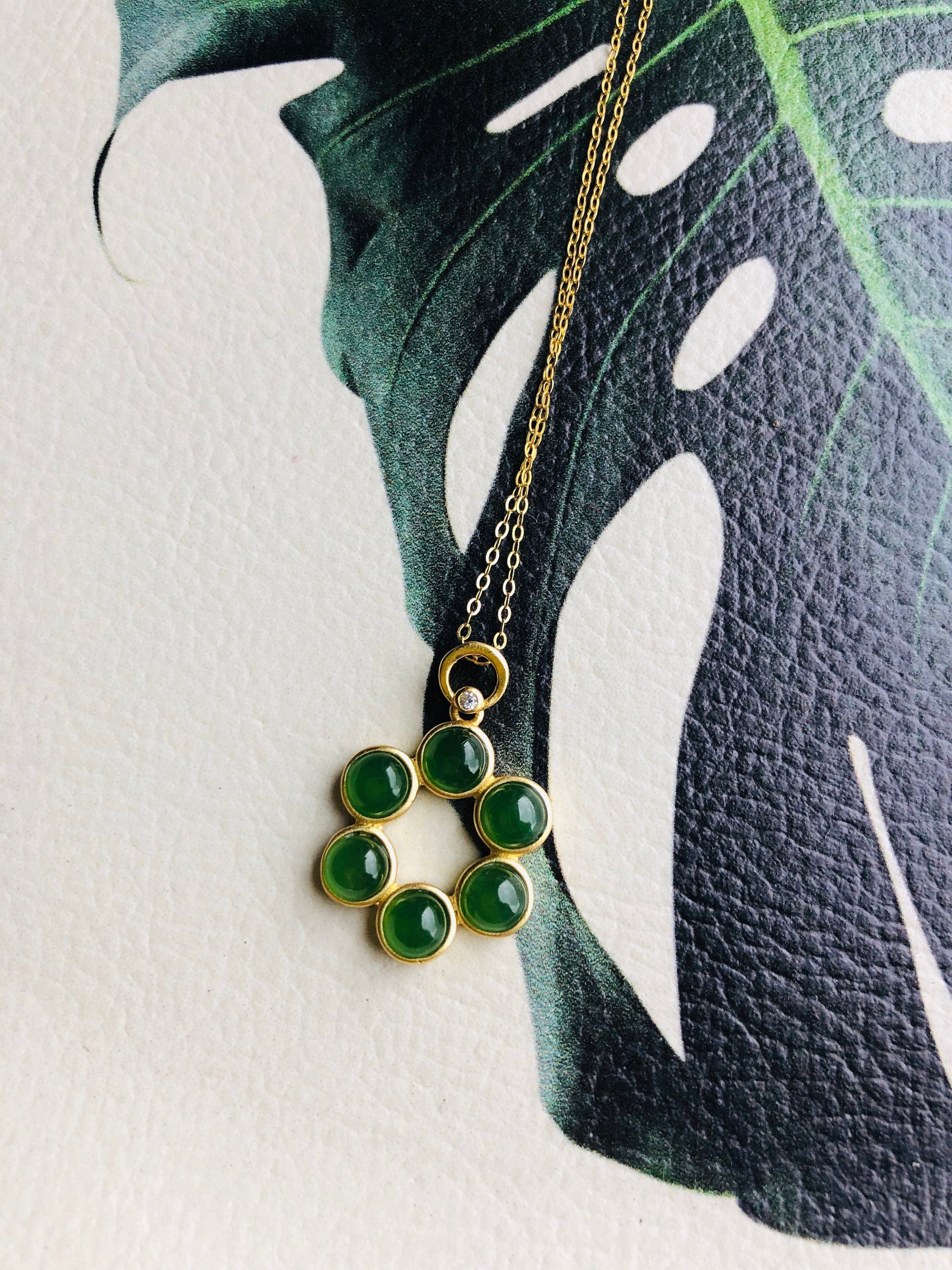 green jade Hexagonal pendant against a textured leather top with leaf picture