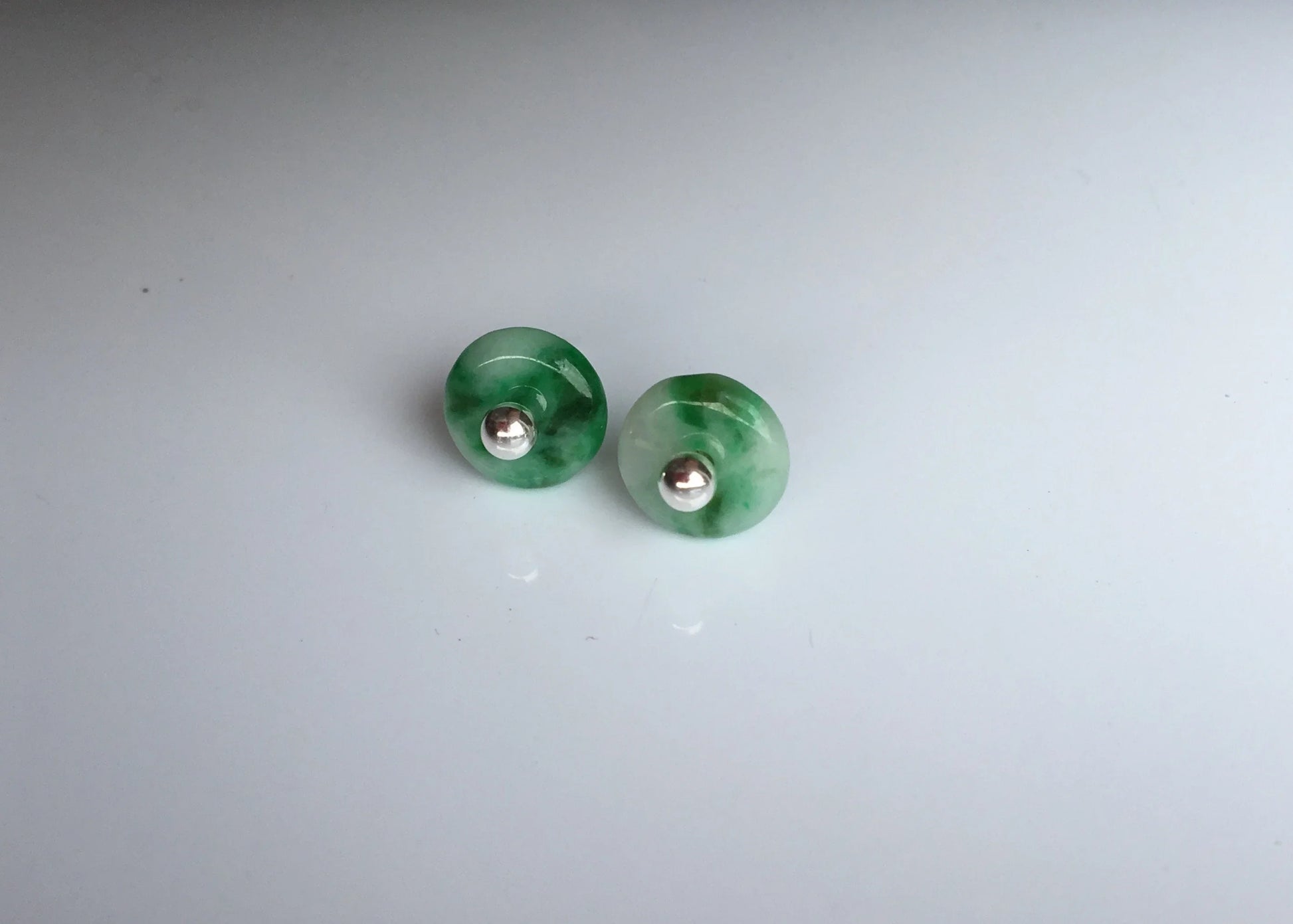 Pair of small green jade circle stud earrings on a light gray background