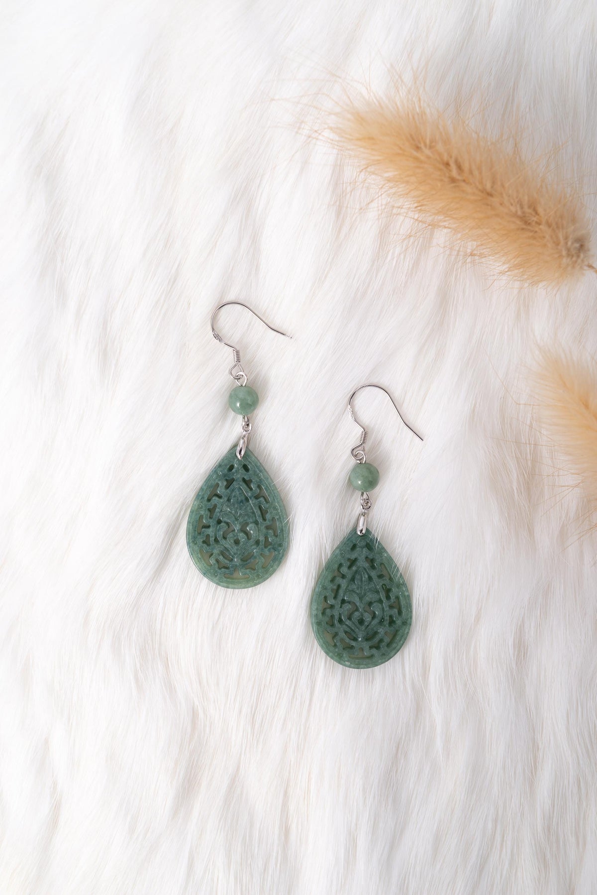 Light green jade teardrop earrings with silver lace frame displayed on a white fur