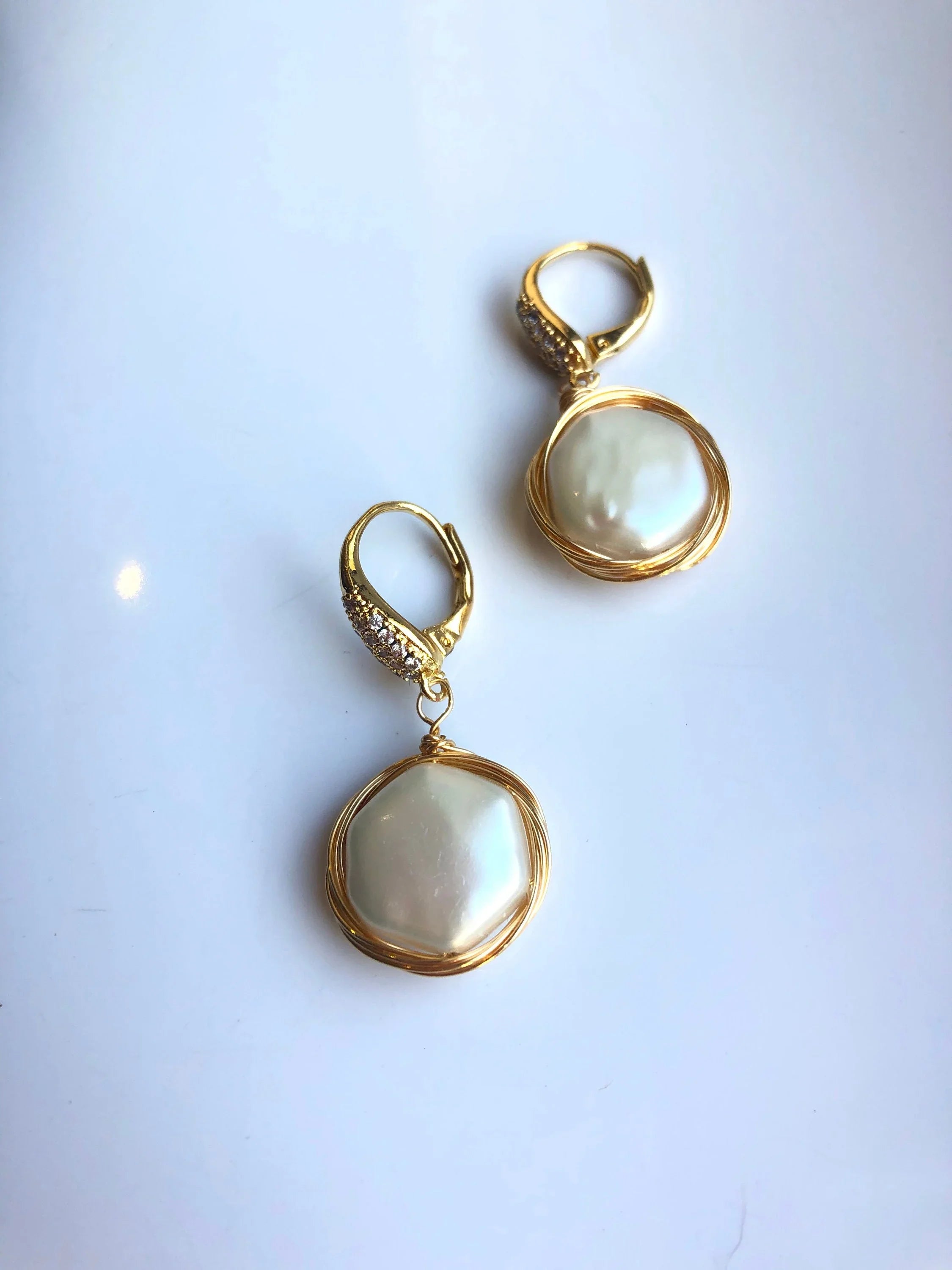 Gold earrings with white stones on a light blue background