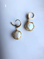Gold earrings with pearl drops on a light gray background with clip details