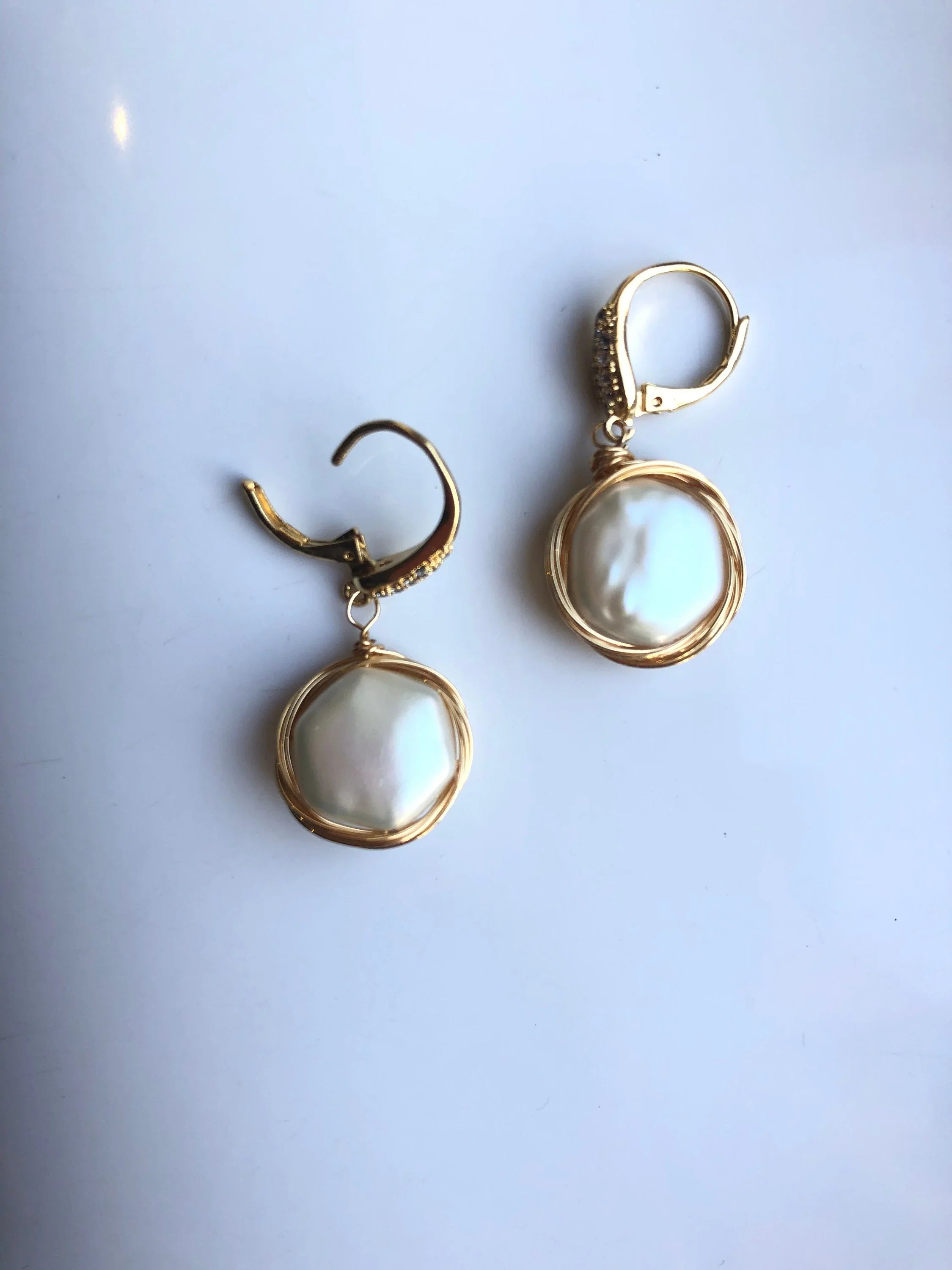 Gold earrings with pearl drops on a light gray background with clip details
