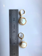 Gold earrings with circular designs on a white surface next to a ruler for scale.