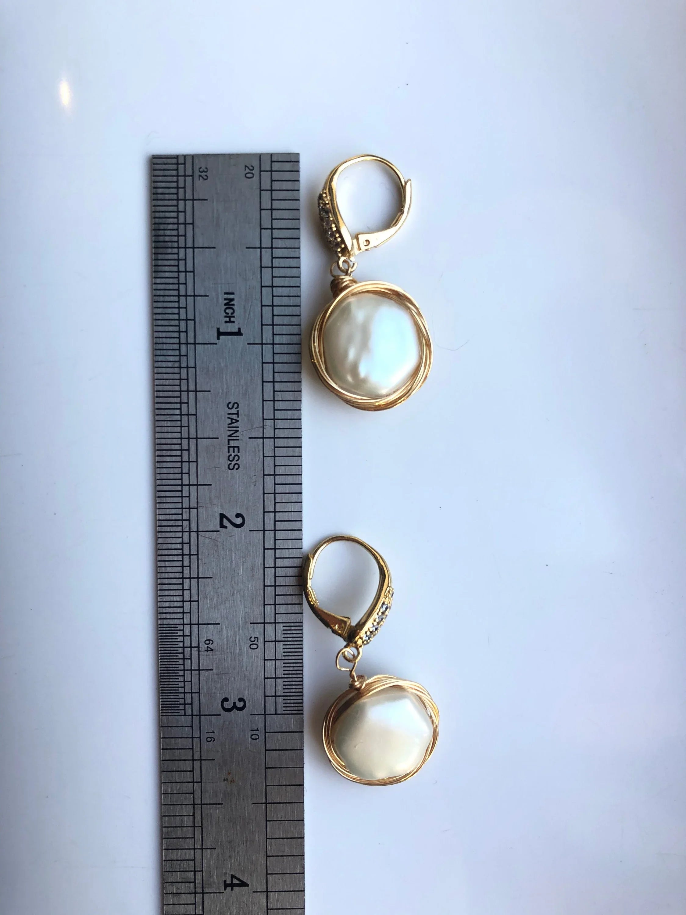 Gold earrings with circular designs on a white surface next to a ruler for scale.