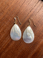 Teardrop-shaped pearl earrings on a wooden surface