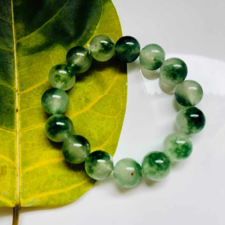Side angle of Chinese jade bracelet with round moss agate beads and elastic cord on a leaf