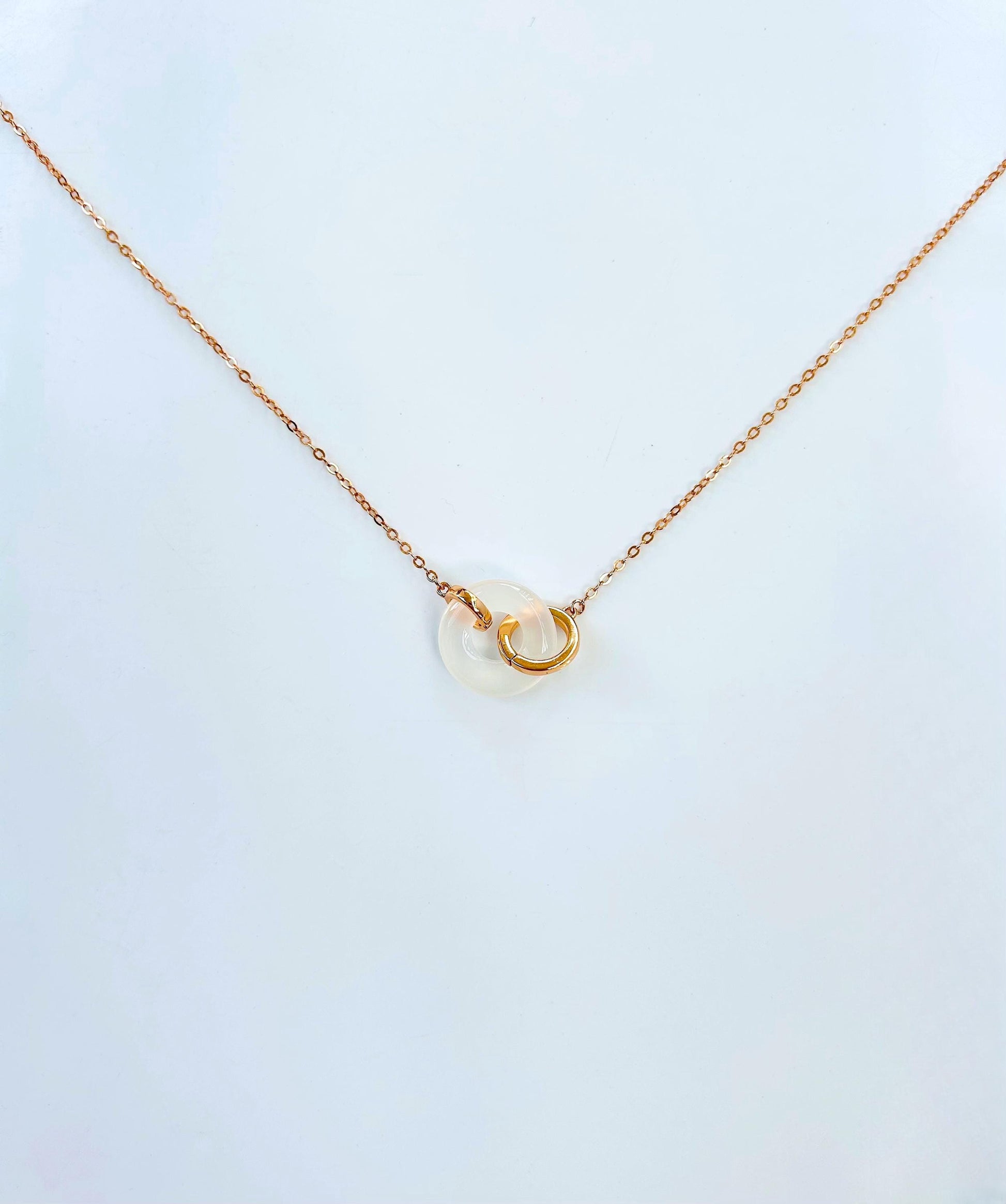 Side angle showing polished white jade circle pendant and rose gold chain

