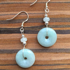 Sage green jade donut earrings in sterling silver dangle style, front view on wood
