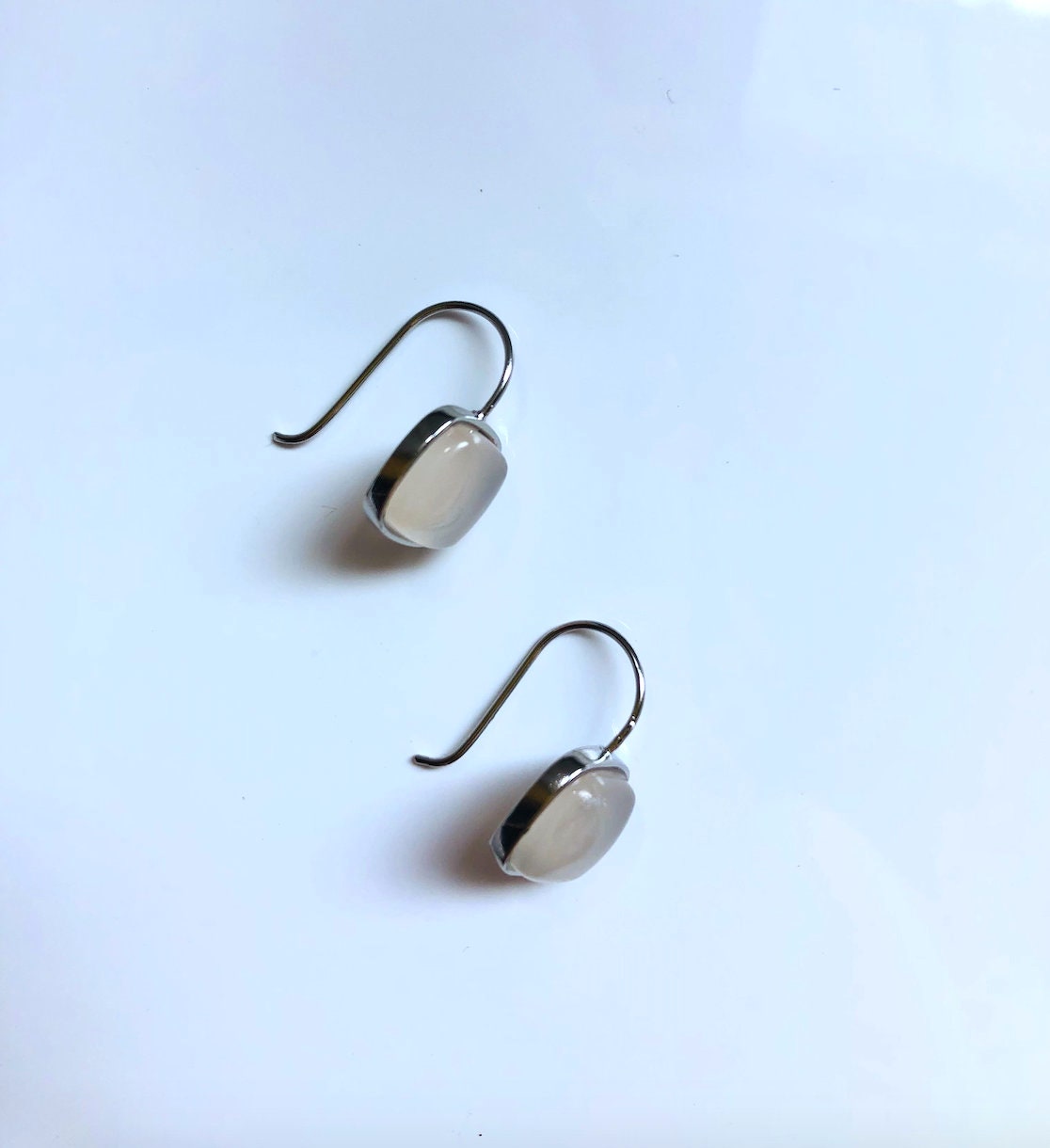 Side view of white jade square dangle earrings hanging from polished 990 silver hooks