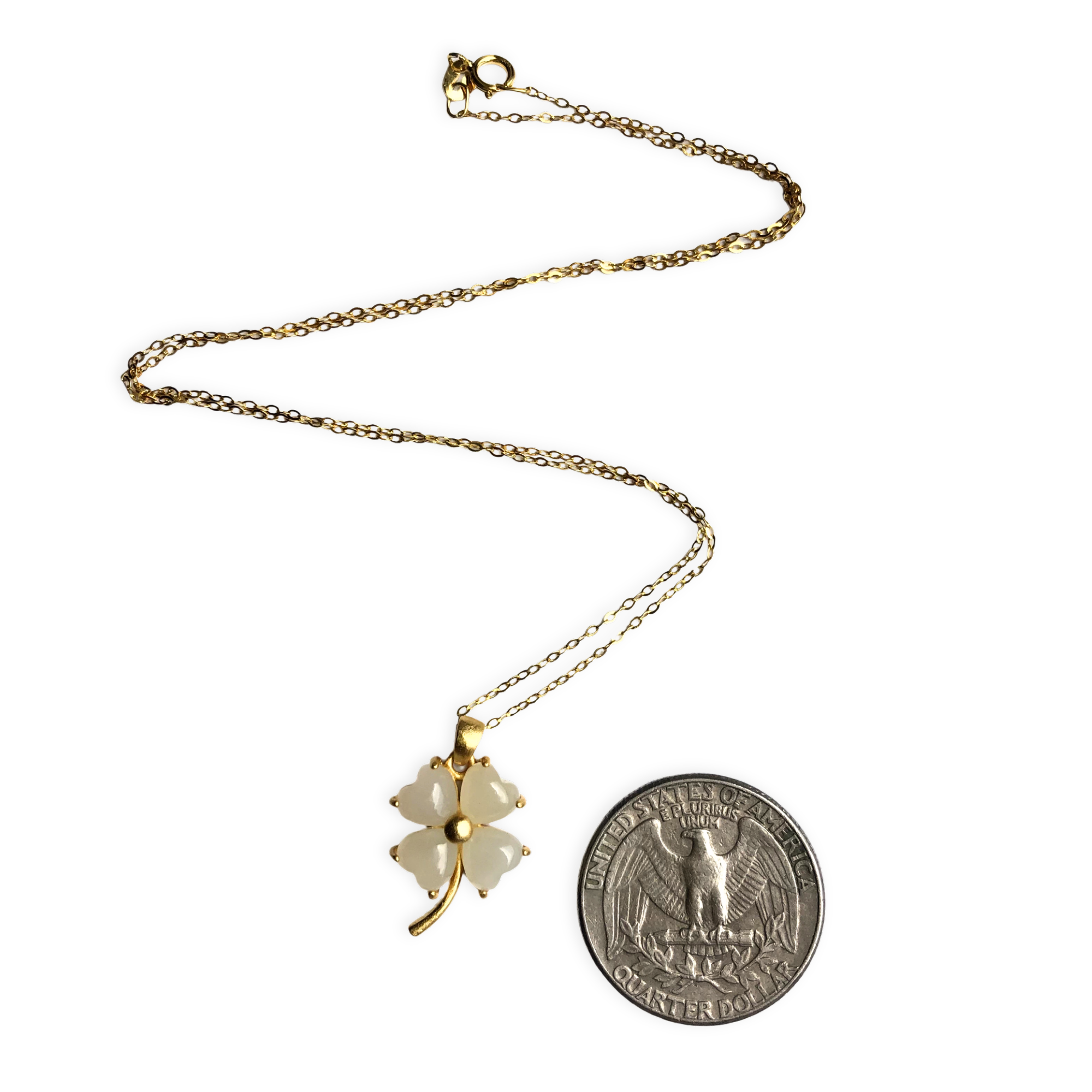 Gold necklace with a four-leaf clover pendant next to a quarter for scale on a white background
