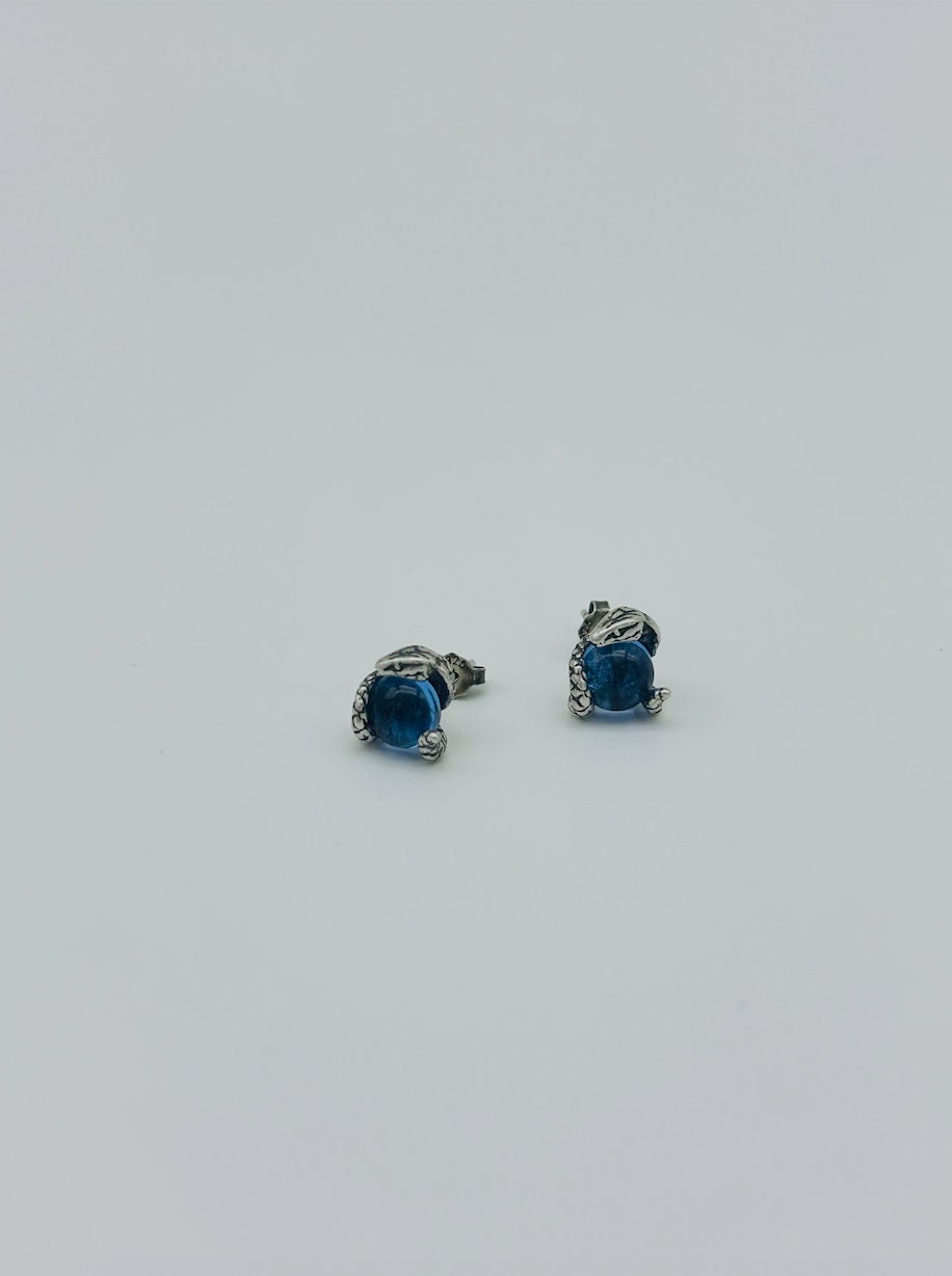 Side view of small silver snake eye studs with deep blue topaz-style gemstone center