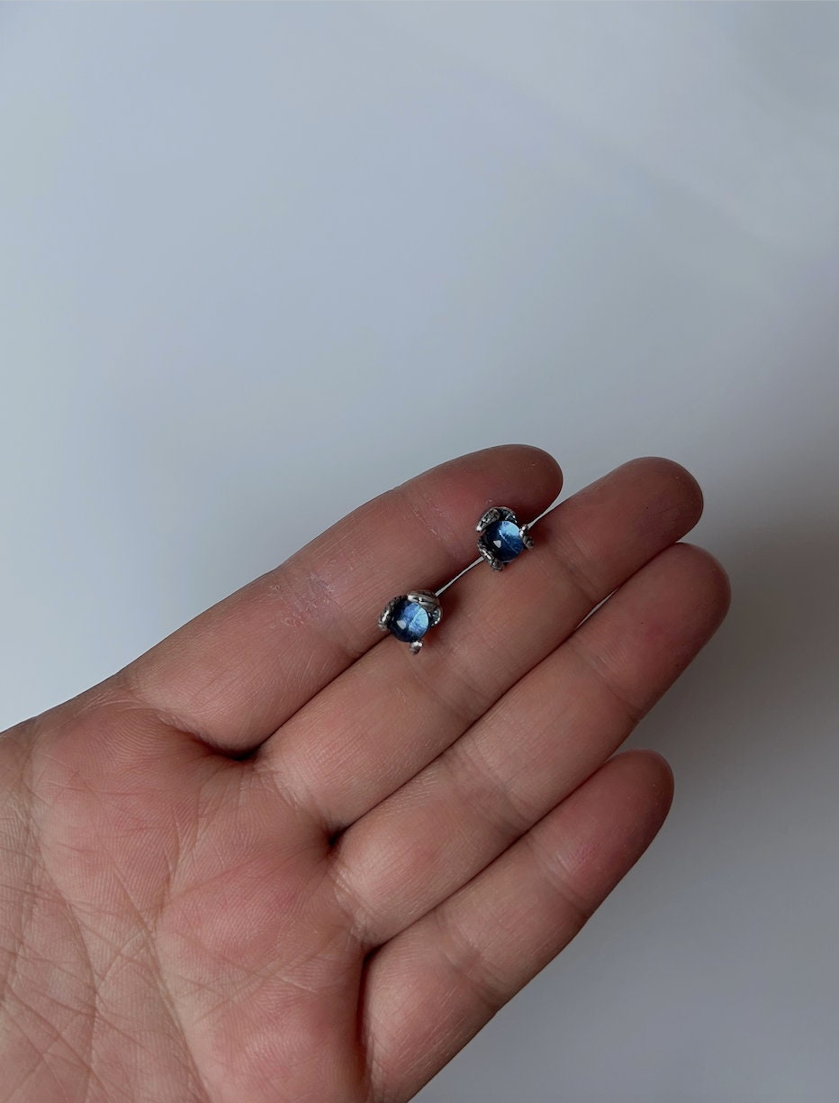 Tiny blue snake eye stud earrings shown in hand for size comparison