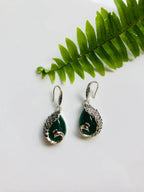 Dark green jade peacock earrings in a silver vintage style displayed with a green leaf