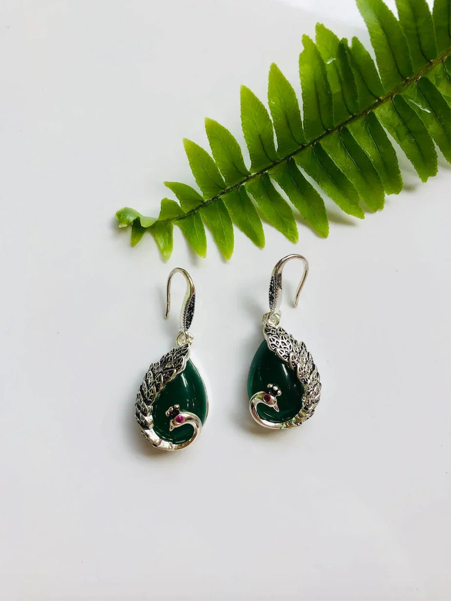 Dark green jade peacock earrings in a silver vintage style displayed with a green leaf