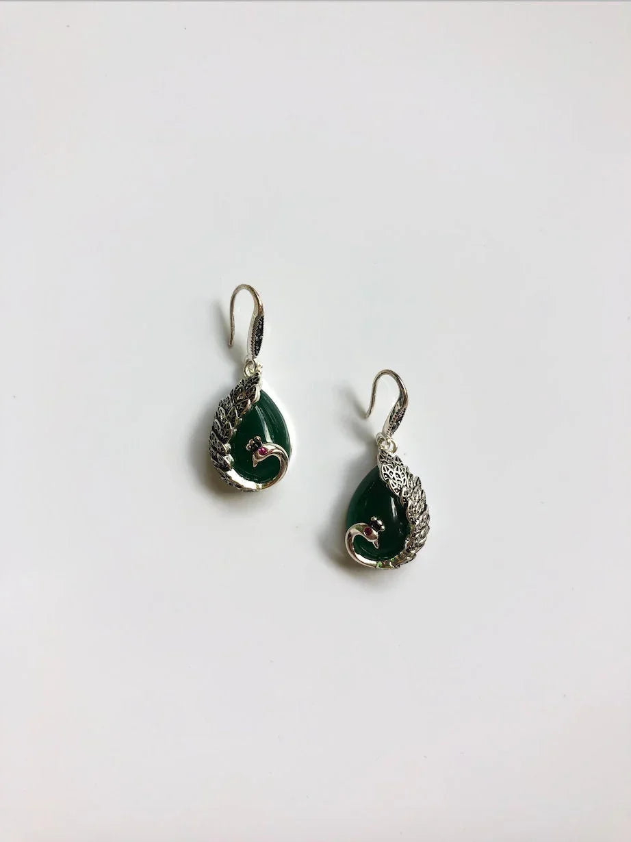 Side angle of silver peacock earrings with dark green jade teardrop stones