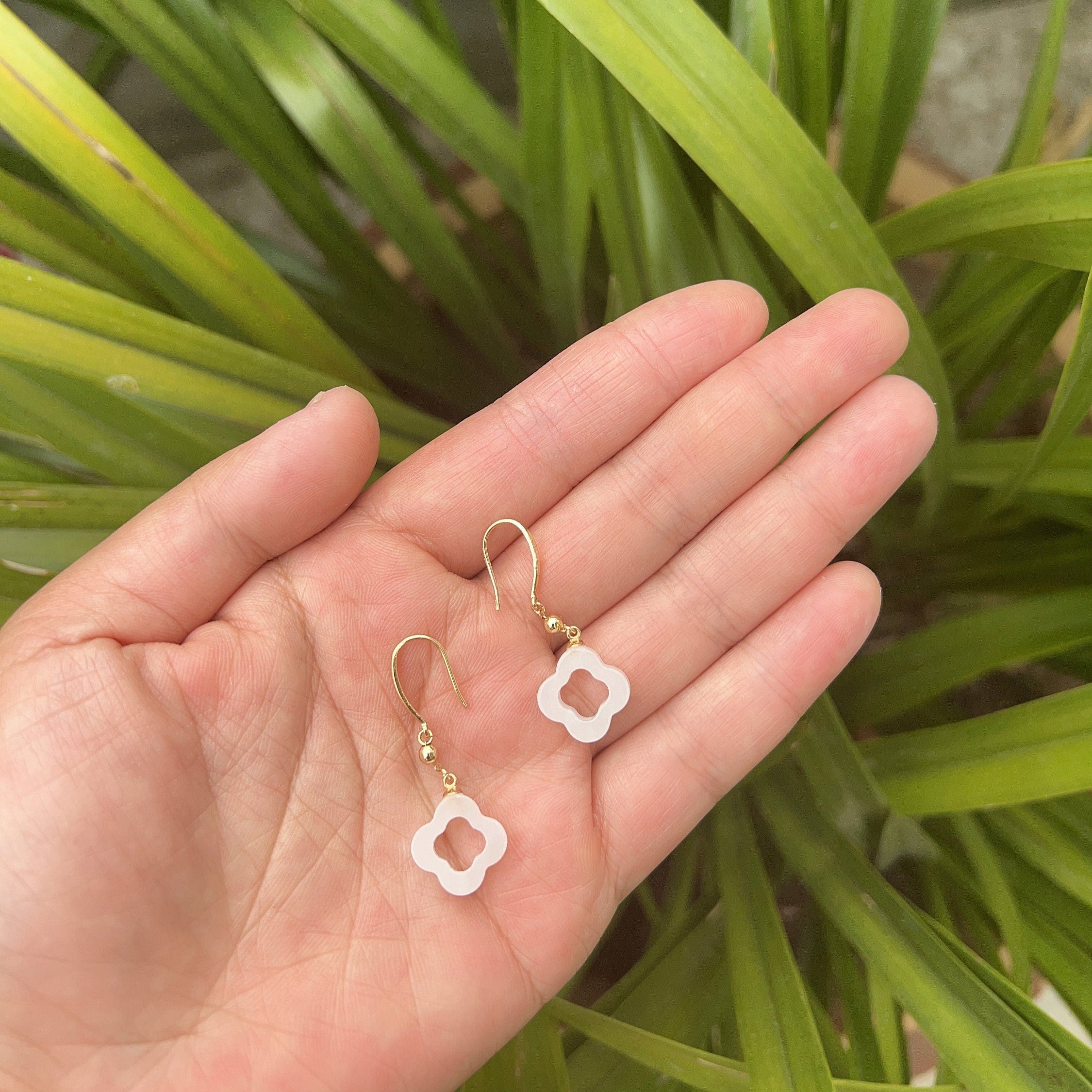 Front view of white jade clover earrings with gold-plated hooks and polished finish on a hand