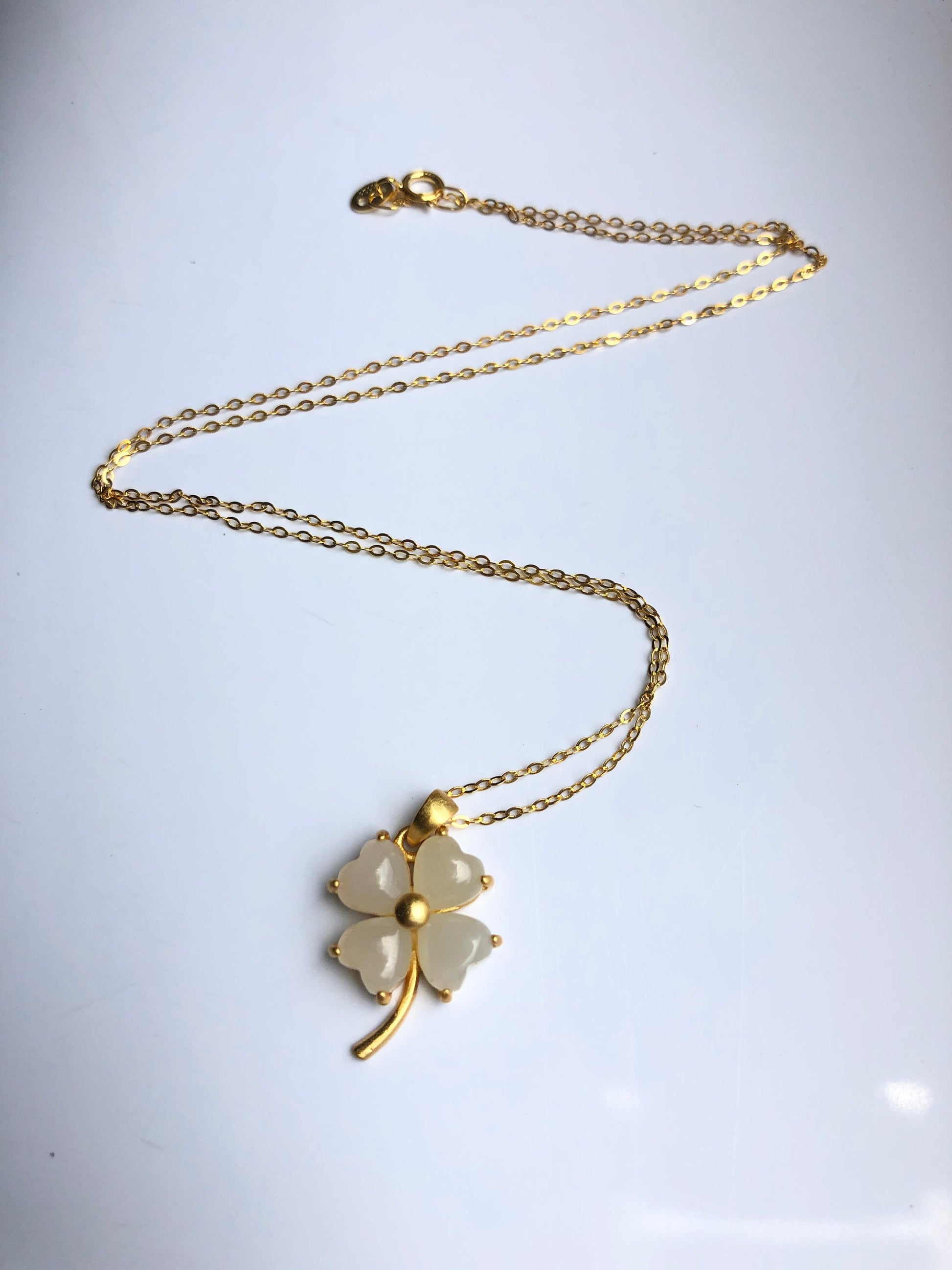 a full view showing white jade clover pendant and delicate gold chain

