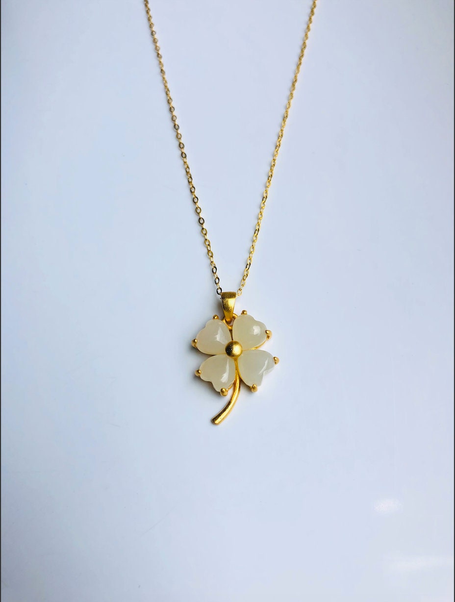 A white jade clover pendant on a gold-plated chain necklace against a white background.
