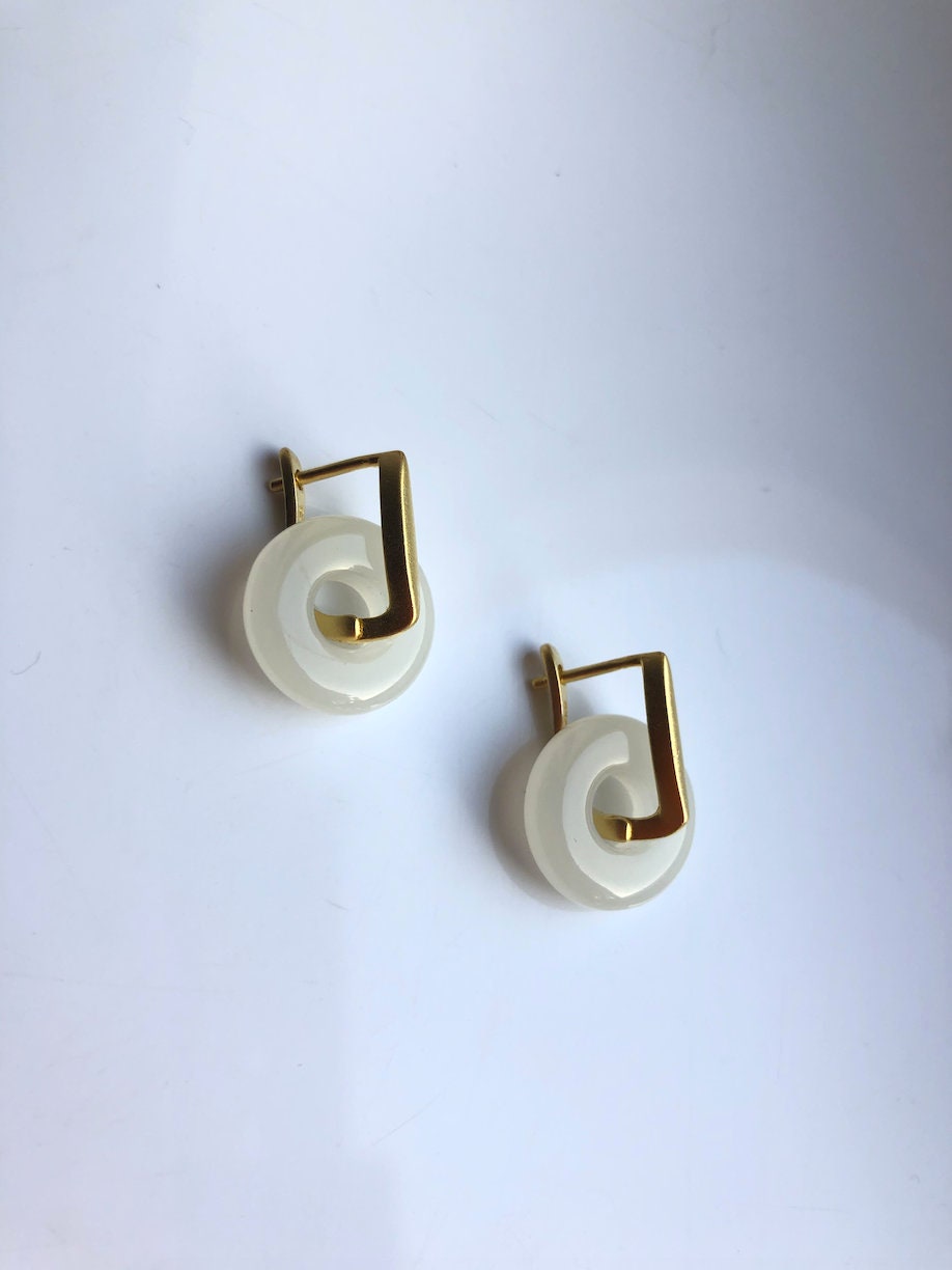 Close-up of minimalist white jade and 18k gold earrings with smooth finish

