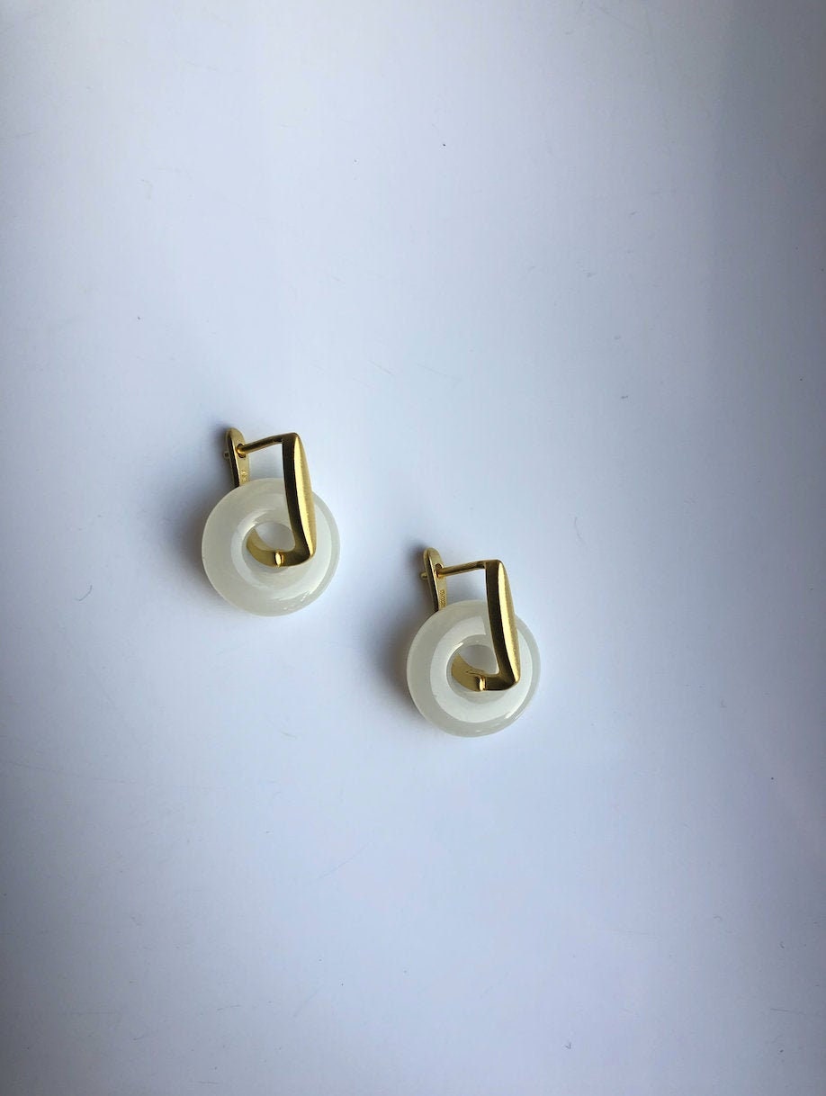 A pair of gold hanging jade earrings with a white jade and gold color design in a modern circular style.