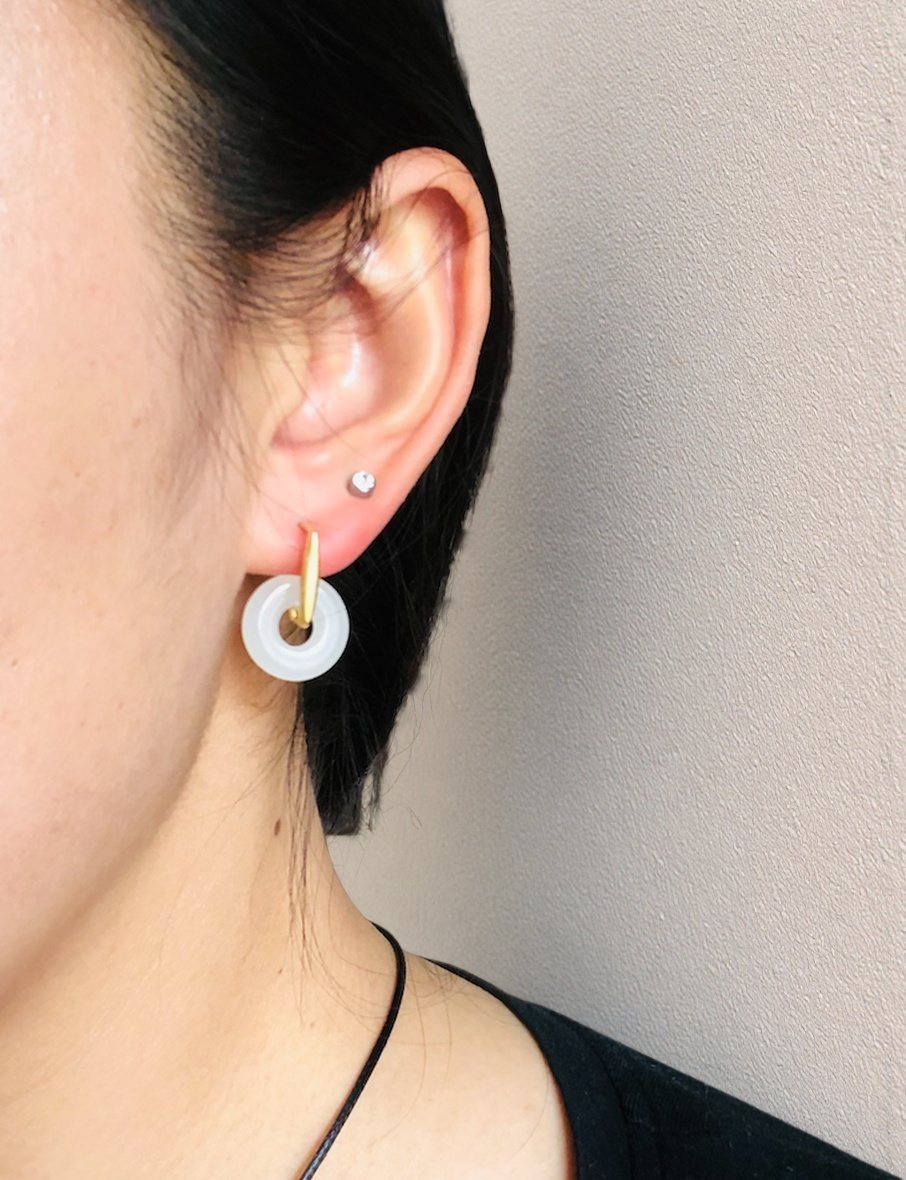 Close-up of an ear wearing a gold hoop earring with a white circular pendant against a neutral background