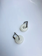 Pair of earrings with white circular pendants and silver accents on a light gray background