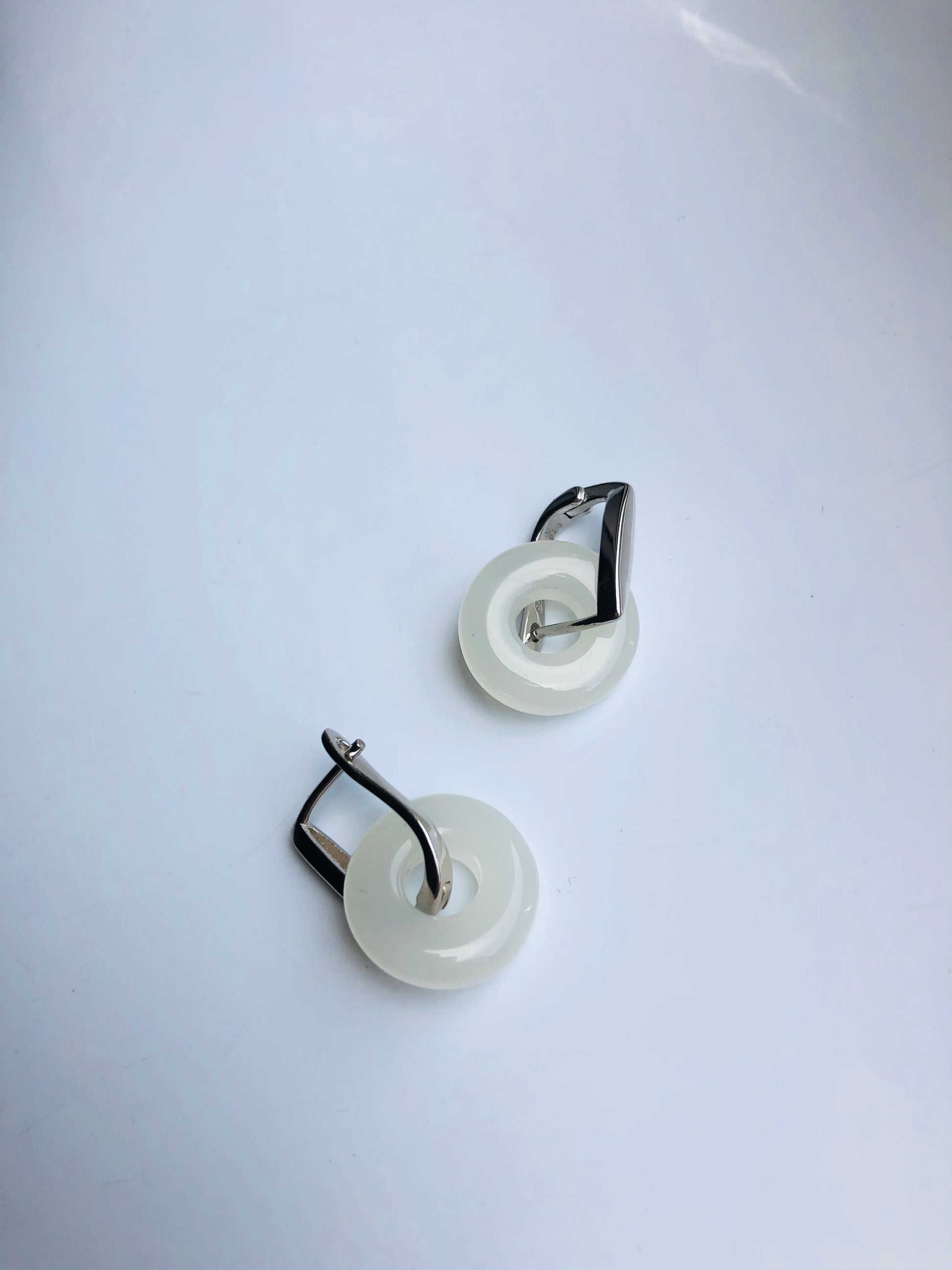 Pair of earrings with white circular pendants and silver accents on a light gray background