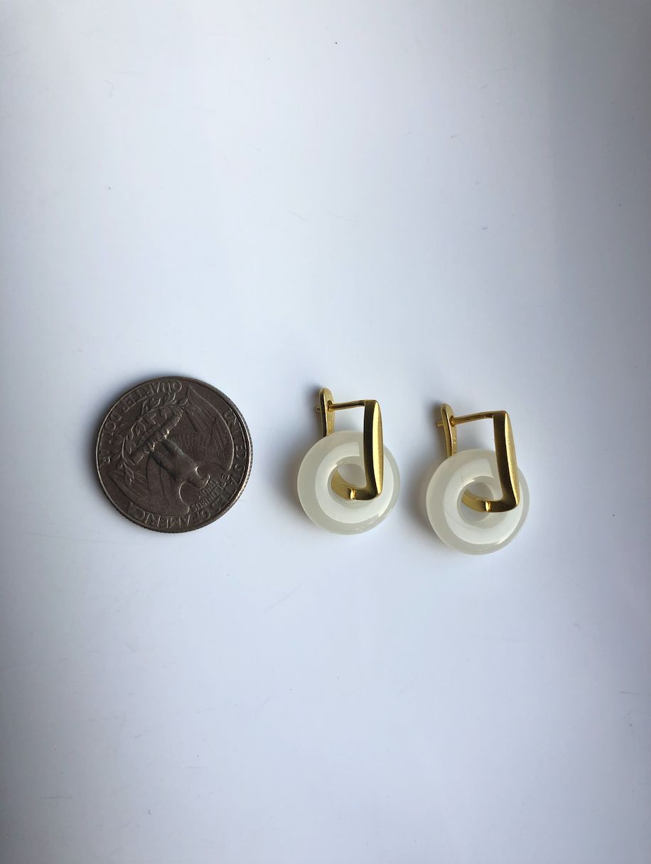 Pair of gold and white hoop earrings next to a coin for scale on a light gray background