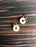 Pair of earrings with gold loops and white circular stones on a wooden surface