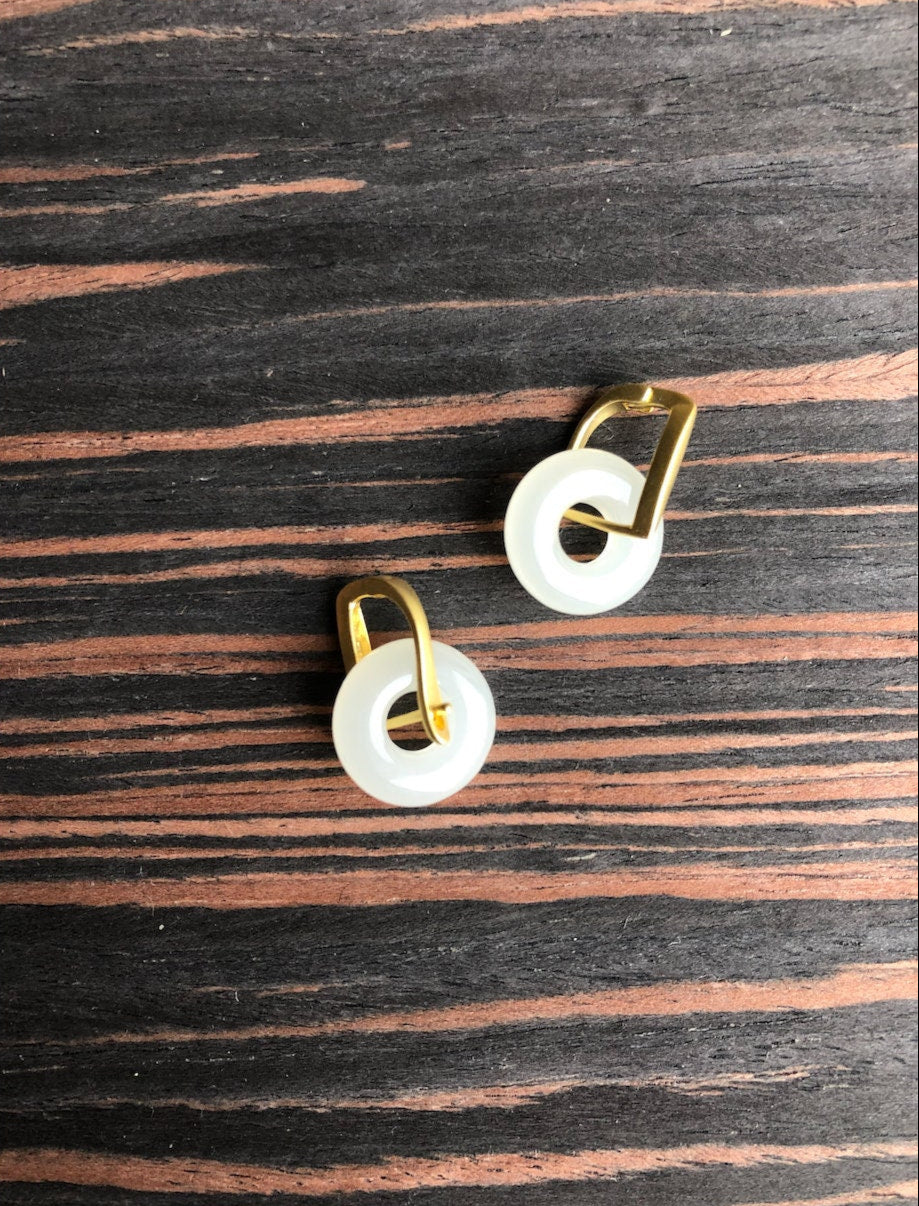 Pair of earrings with gold loops and white circular stones on a wooden surface