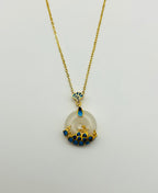 A white jade circular pendant necklace with 18k gold plating and blue wave detailing on the ceramic, displayed against a white background.