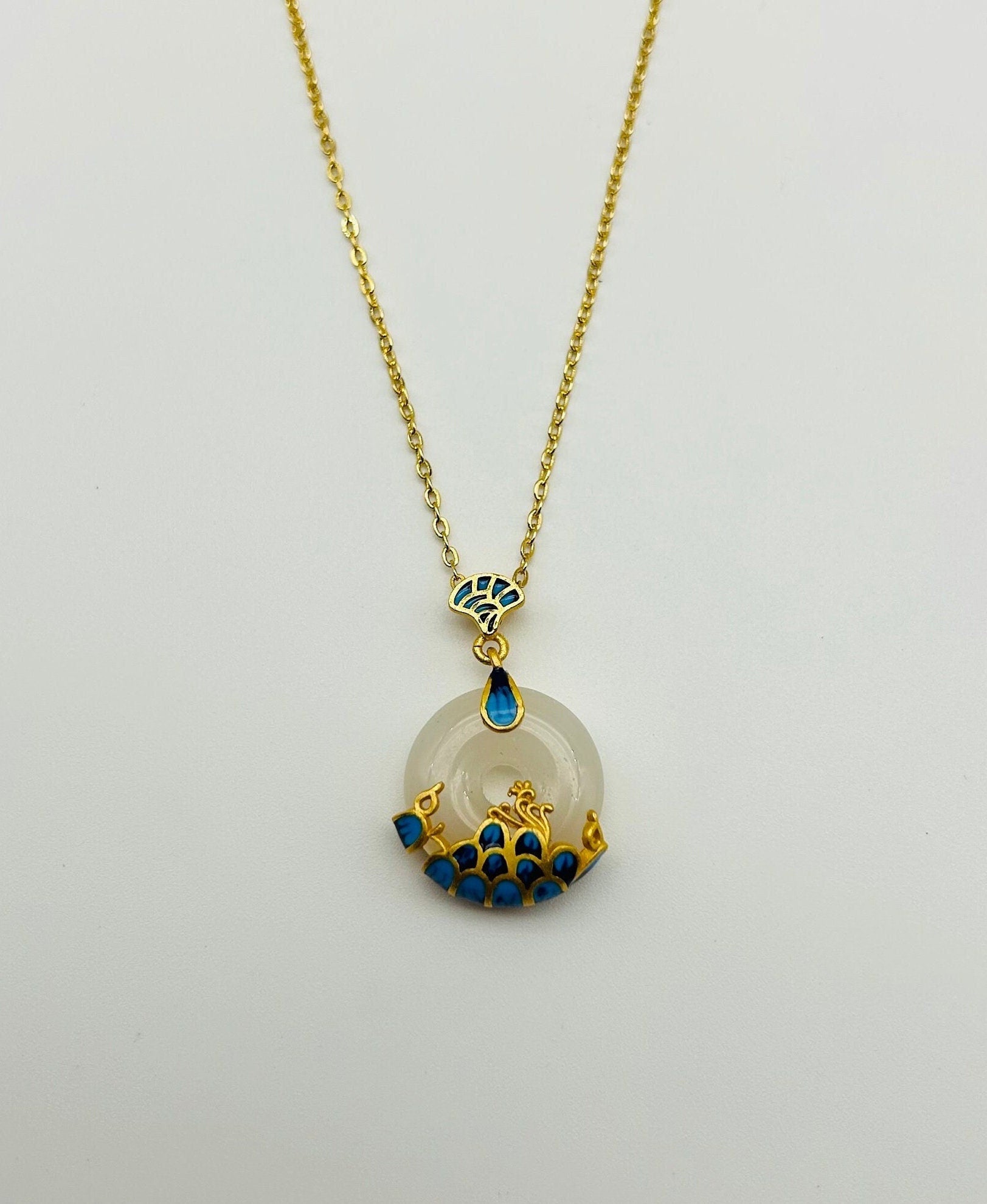 A white jade circular pendant necklace with 18k gold plating and blue wave detailing on the ceramic, displayed against a white background.