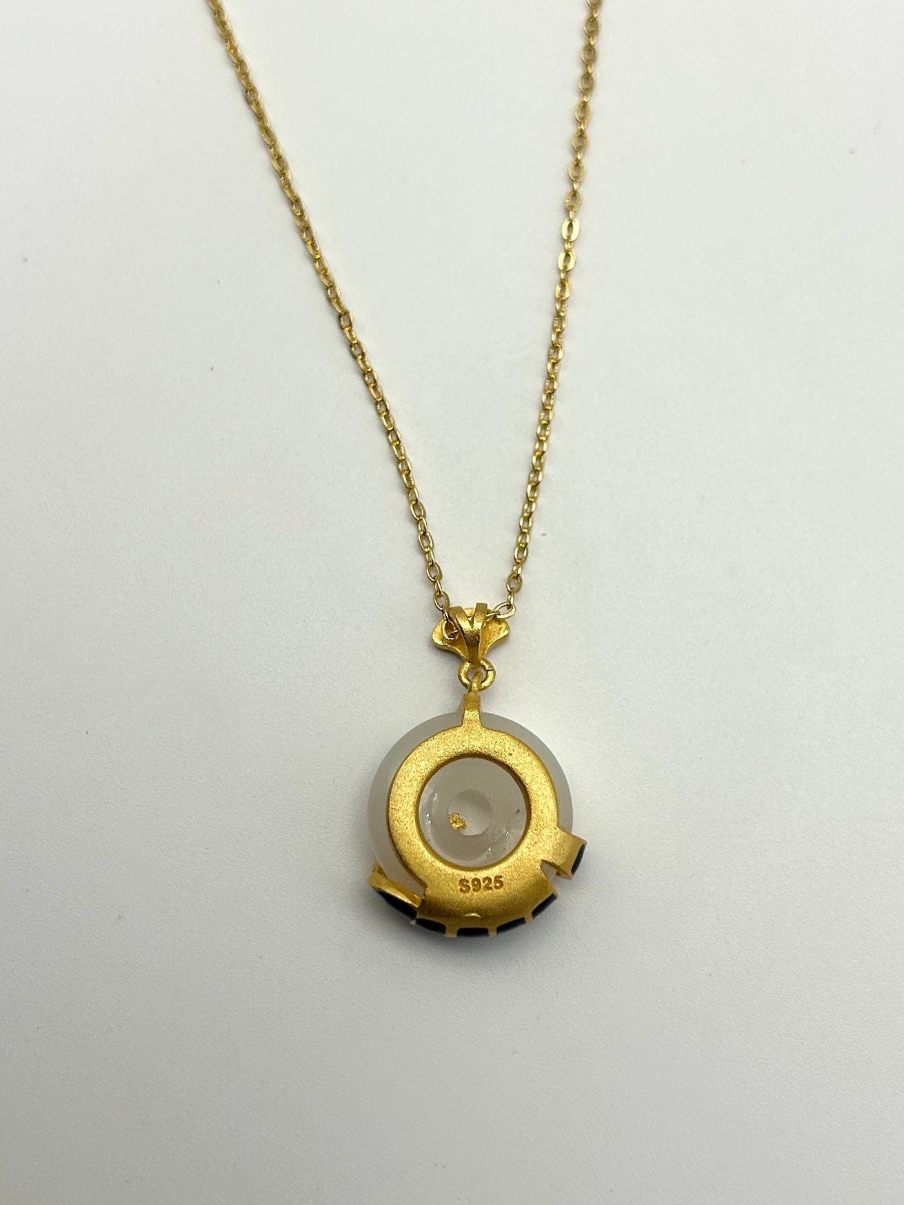 Back of white jade pendant showing smooth finish, S925 mark and gold setting

