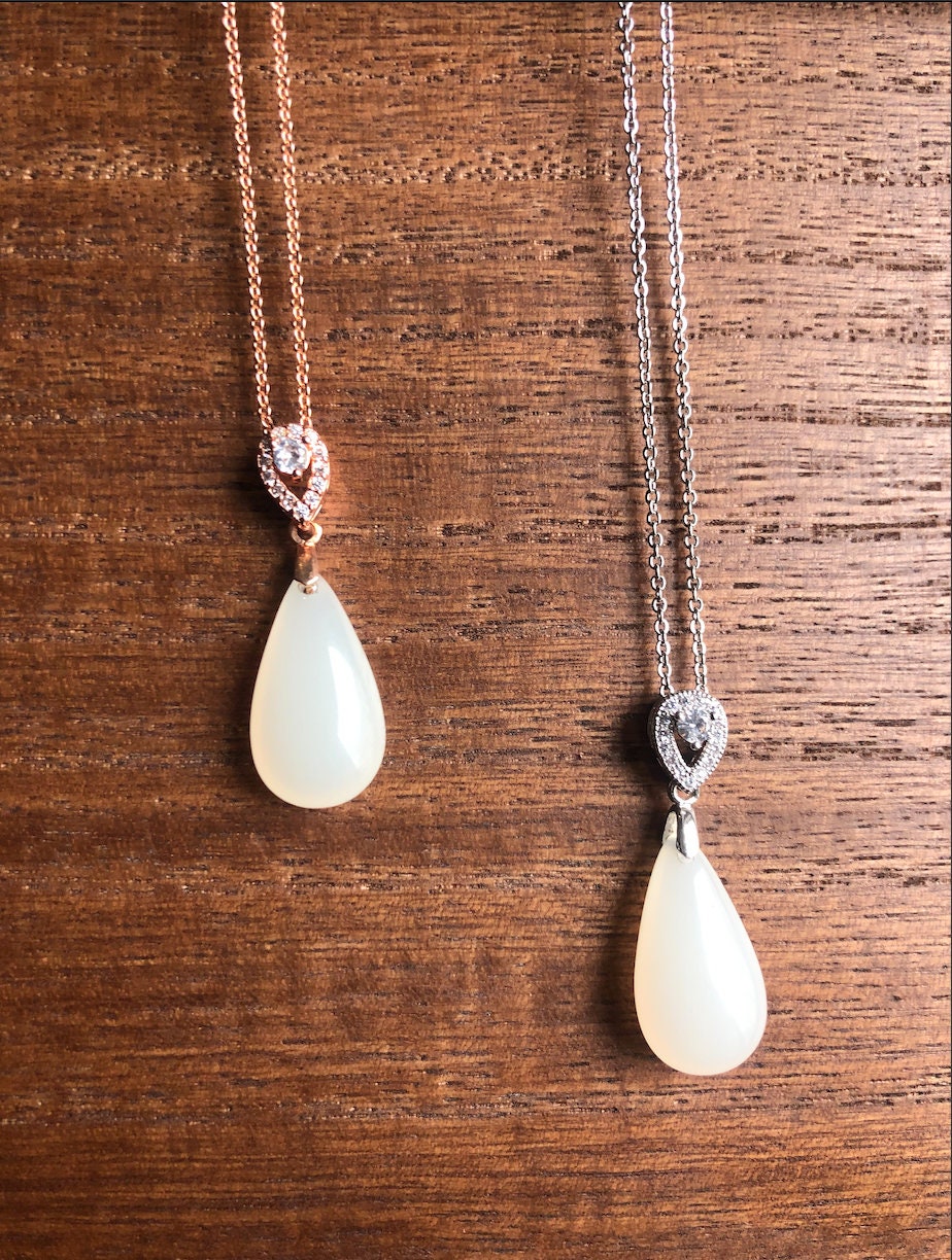 Detail view of white jade pendant paired with elegant rose gold chain and silver chain, in a pair on wood