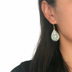 Close-up of a person wearing a white teardrop earring with gold hook on a plain background