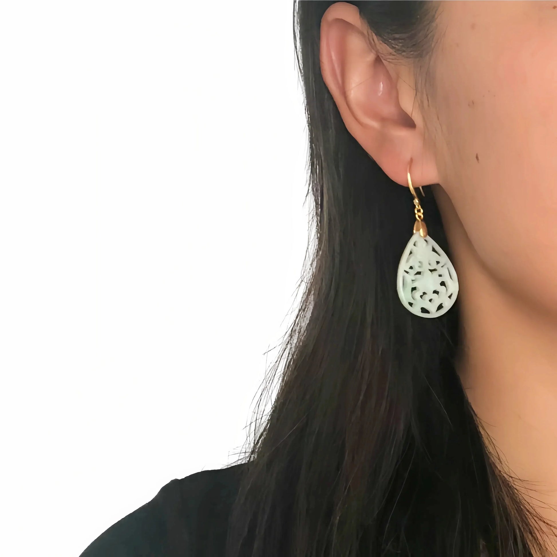 Close-up of a person wearing a white teardrop earring with gold hook on a plain background