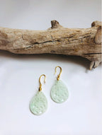 Teardrop-shaped lace earrings with gold hooks on a white background with a piece of driftwood.